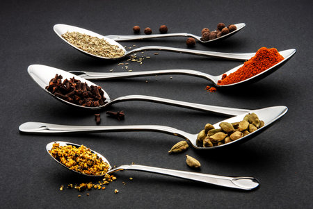 spices in metal spoons on a black background