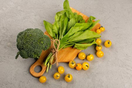 a front view broccoli green leafs along with yellow tomatoes on the gray background