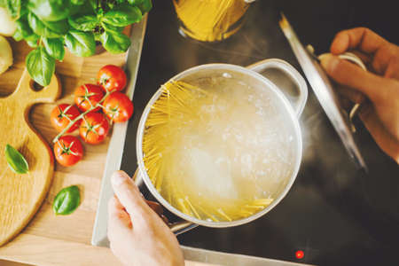 Process of cooking homemade italian pasta. Lifestyle background. Man dropping spaghetti into boiling water. Closeup. Horizontal.の写真素材
