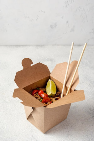 Take-out noodles in paper box with chopsticks on light backgroundの写真素材