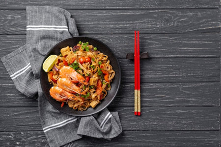 Stir fry noodles with shrimps and vegetables in a black bowl on a black wooden background, top viewの写真素材