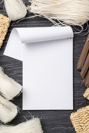 Blank sheet of paper, noodles and chopsticks on wooden background