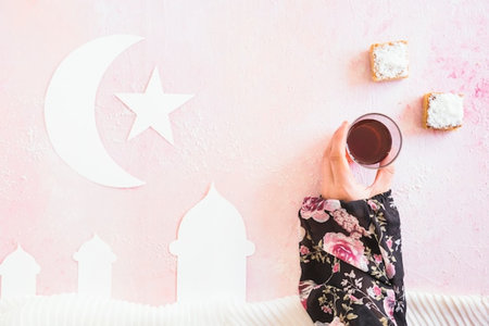 Woman hand holding cup of coffee on pink background, Ramadan Kareem concept