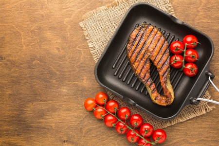 Grilled pork steak on a grill pan with tomatoes on wooden backgroundの写真素材