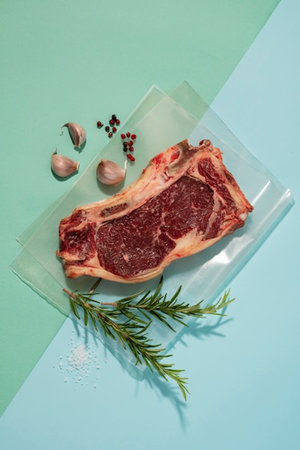 Raw ribeye steak with rosemary and garlic on a blue background