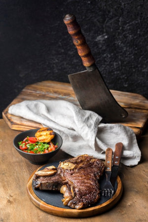 Grilled beef steak with vegetables on wooden board over dark background.の写真素材