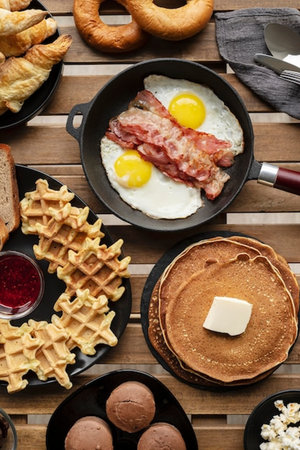 Delicious breakfast with fried eggs, bacon and waffles on wooden table