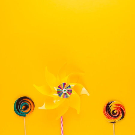 top view of colorful lollipops and pinwheel on yellow backgroundの写真素材