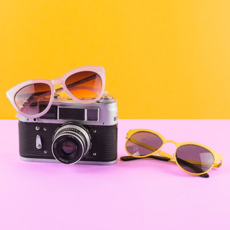 Retro film camera with sunglasses on pink and yellow background. Minimal summer concept.の写真素材