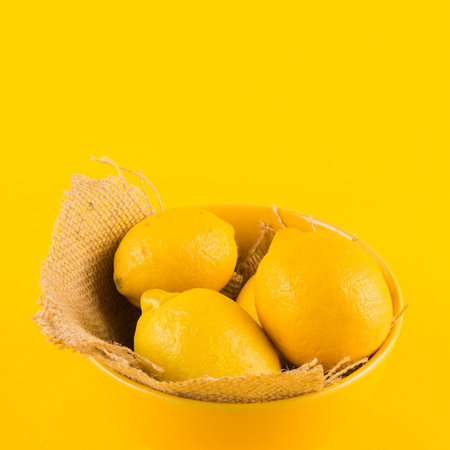 Lemons in a bowl on a yellow background with copy space