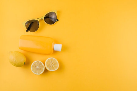 Sunblock bottle with sunglasses and lemon on yellow background. Summer concept.の写真素材