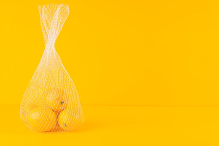 Lemons in a mesh bag on a yellow background. Copy space.の写真素材