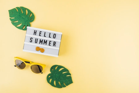 Hello Summer text on lightbox with sunglasses and monstera leaf on yellow backgroundの写真素材