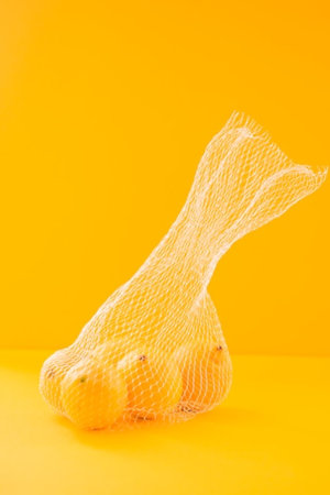 Lemons in a mesh bag on a yellow background. Copy space.の写真素材