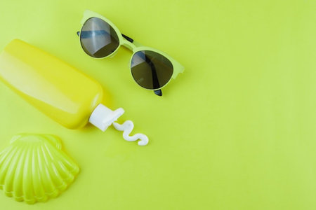 Sunscreen bottle and sunglasses on green background. Sun protection concept.