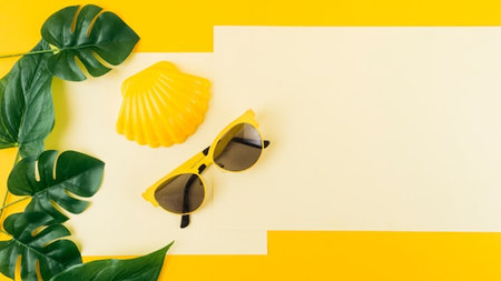 Summer background with sunglasses, monstera leaves and yellow paper sheet on yellow backgroundの写真素材