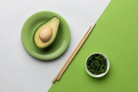 Sliced avocado and chopsticks on green and white background, top view