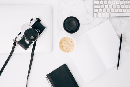 Top view of modern workspace with camera, notebook and coffee cup on white marble table