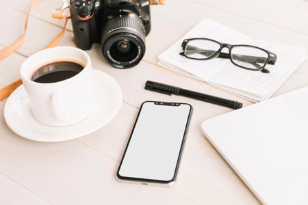 Smartphone with blank screen, coffee cup, camera and notebook on wooden tableの写真素材