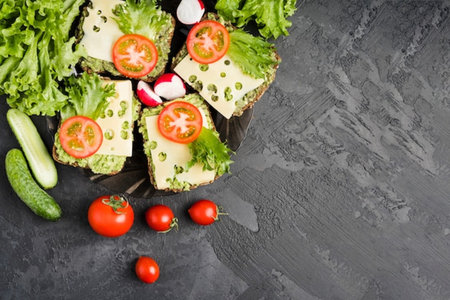 Healthy vegetarian sandwiches with avocado, cucumber, radish, lettuce and tomatoes on black stone background. Top view with copy spaceの写真素材