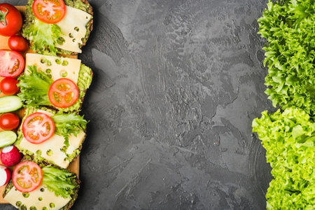 Sandwiches with cheese, tomatoes, cucumbers and lettuce on black stone background. Top view with copy spaceの写真素材