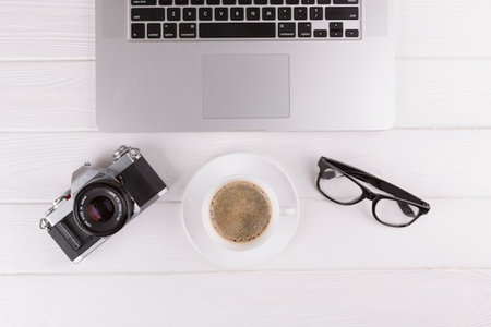 Top view of laptop, camera and coffee cup on white wooden tableの写真素材