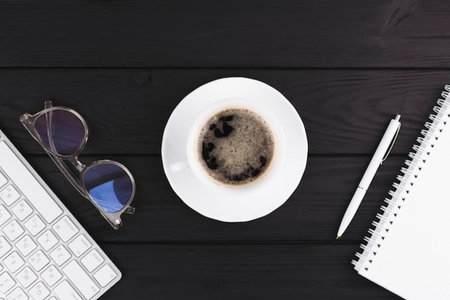 Office desk table with keyboard, coffee cup, notebook and glasses. Top view with copy space