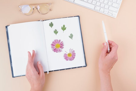 Flat lay of female hands drawing flowers in notebook with white keyboardの写真素材