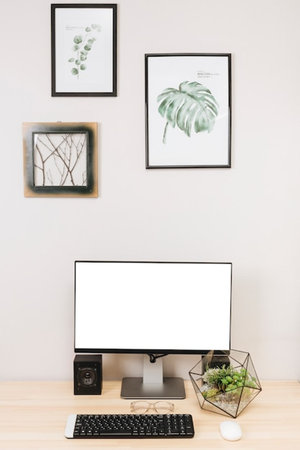 Modern workspace with blank screen computer, keyboard, coffee cup, plant and picture frame on white...