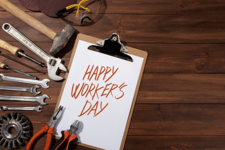 top view of happy workers day lettering on clipboard with tools on wooden background