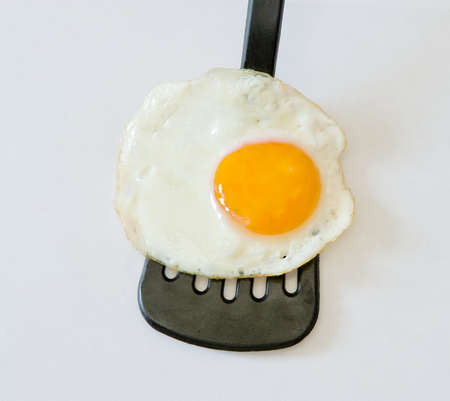 Close up of fried egg on plastic spatula on a white backgroundの写真素材