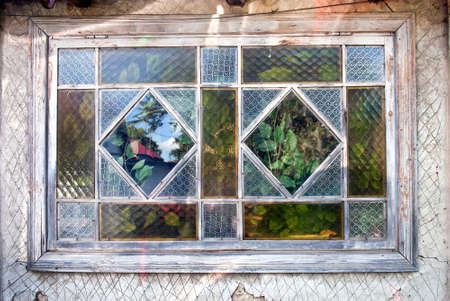 Old window with stained glass of rustic cottage, reflections and green plantsの写真素材