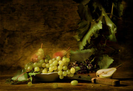 Still life of grapes and pears on a dish with knife and vine in the background, looking like a painting. Artistic blurの写真素材