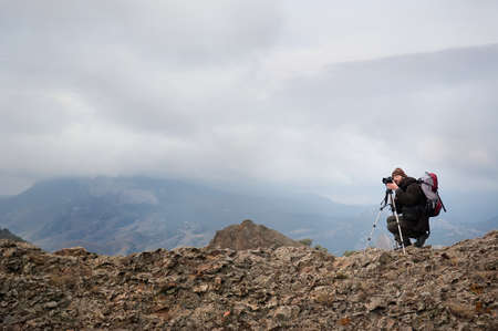 Professional photographer takes photos with camera on tripod on rocky peak.の写真素材