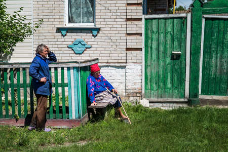 Sumy, Ukraine - Jule 6, 2017: Unidentified old woman knit the traditional wool sock for winter and her husband in front of their brick house.のeditorial素材