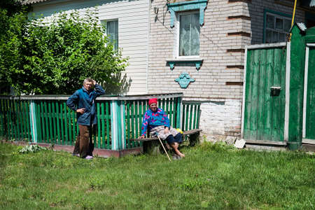 Sumy, Ukraine - Jule 6, 2017: Unidentified old woman knit the traditional wool sock for winter and her husband in front of their brick house.のeditorial素材