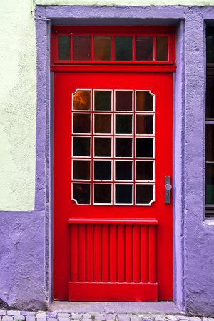 Wooden red beautiful door in an old lilac, white colored buildingの写真素材