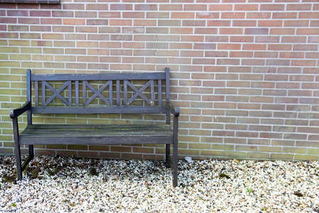 Old wooden bench and colorful pebbles against a brick wallの写真素材