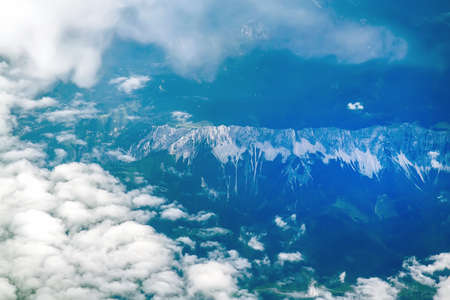 View of the Earth from the airplane flying above the clouds at high altitude over the mountains. Selective Focusの写真素材