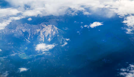 View of the Earth from the airplane flying above the clouds at high altitude over the mountains. Selective Focusの写真素材