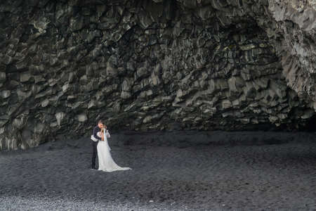 Reynisfjara Beach, Spain - July 13, 2019: happy wedding couple kissing on background of Reynisfjara Beach. Selective focusのeditorial素材