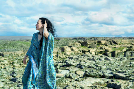 Women in a blue dress fluttering in a wind standing on a lava rocks field pn west Icelandの写真素材