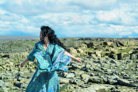 Women in a blue dress fluttering in a wind standing on a lava rocks field pn west Icelandの写真素材