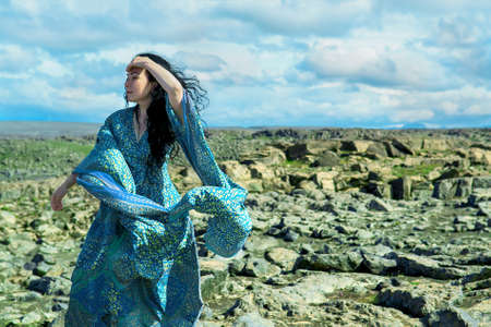 Women in a blue dress fluttering in a wind standing on a lava rocks field pn west Icelandの写真素材