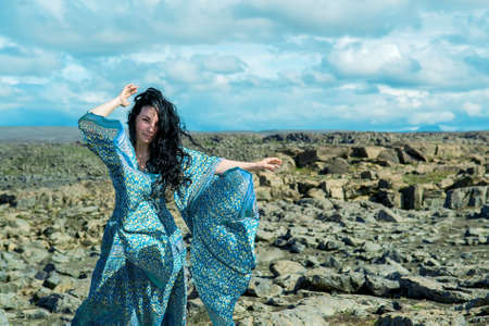 Women in a blue dress fluttering in a wind standing on a lava rocks field pn west Icelandの写真素材