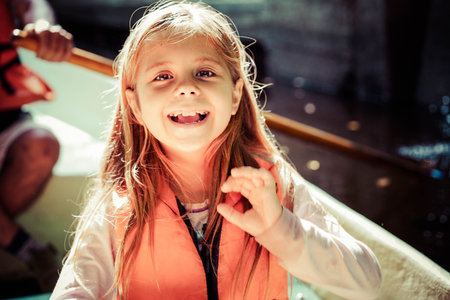 A girl in a life jacket rides a boat in the park on a sunny day. The concept of child safety and...