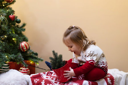 A child in winter Christmas red clothes holds a small Christmas tree in his hands and plays with toys. The concept of New Year holidays, discounts, shopping.の写真素材