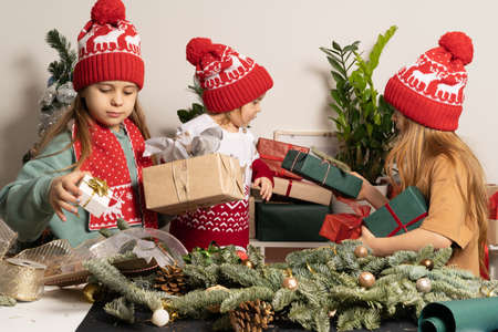 Three children in red Christmas hats are packing gifts and making Christmas decorations. The concept of hobby, family , holidays and holidays and eco-friendly lifestyle.の写真素材