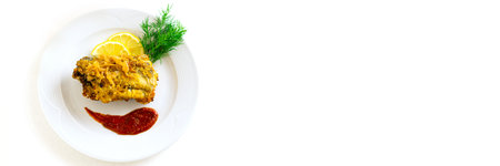 Battered fish on a white ceramic plate with lemon, red sauce and herbs on an isolated white...