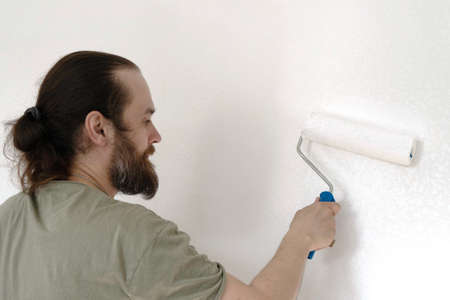 Back of young caucasian man painting white wall with paint roller for home renovation background.の写真素材